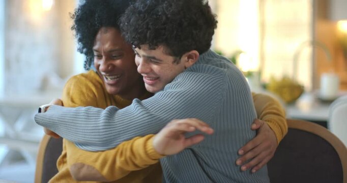 Two African American men hugging, laughing, then showing small red key fob at home dining table