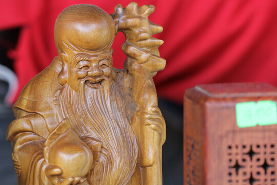 Shou Lao wood carving statue of longevity god on red background, hand carved wooden Ong Tho figure holding immortal peach for feng shui luck home decor, Vietnam