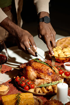 Vertical image of African American man carving roasted turkey during Thanksgiving dinner with friends. Scene represents holiday celebration, suitable for festive food marketing