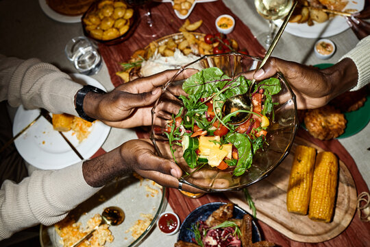African American young adults sharing salad bowl during Thanksgiving dinner at home, celebrating friendship. Image suitable for holiday marketing and diverse lifestyle campaigns, high angle view