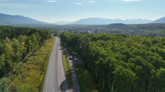 Aerial view of a two-lane road surrounded by dense forest with mountains in the background, clear and balanced framing, natural lighting, evoking tranquility and vastness in New Hazelton.