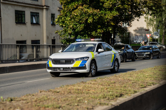 A marked police patrol car drives down a city street with its light bar flashing, other vehicles pulled aside to let it move through traffic ahead of them.