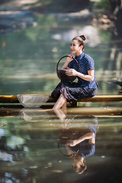 happy Asian women in traditional indigo dress catching fish on a bamboo bridge in Sakon Nakhon, Thailand. Perfect for travel banners and culture ads.