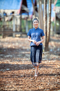 Young happy Asian woman wearing traditional Sakon Nakhon indigo dyed fabric dress walking in countryside, Isan local lifestyle and cultural tourism concept