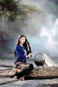 Authentic Thai culture on the Mekong river! Smiling young woman in beautiful Sakhon Nakhon indigo traditional clothing, relaxing with fishing gear. Captures local lifestyle