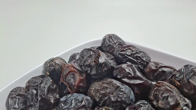 Organic dried dates in white bowl, sweet ajwa date fruit on plain background, healthy ramadan snack for traditional middle eastern cuisine