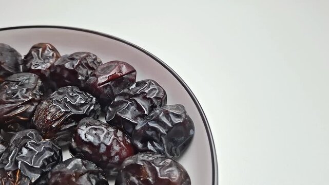 Ajwa dates on ceramic plate, dried black date fruit for Ramadan, organic sweet palm dates snack on white background