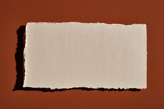 Torn recycled paper sheet with rough edge on brown background