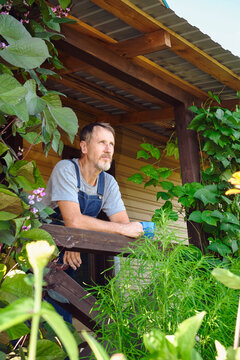 Man enjoying hot beverage on his rural porch surrounded by lush greenery