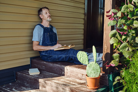 Man in overalls enjoying peaceful rest with book on sunny house porch