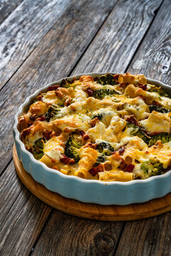 Pasta casserole with broccoli and smoked bacon on wooden table
