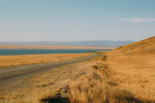 Long empty asphalt road running alongside river Irtysh shore through dry steppe hills in East Kazakhstan.