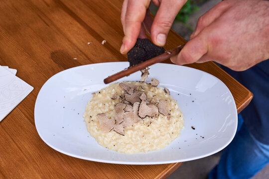Chef Shaving Black Truffle Over Fresh Risotto on White Plate in Restaurant