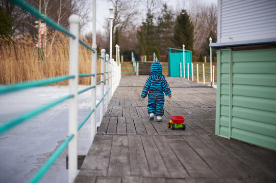 Toddler in Blue Overalls Pulling Toy Cart on Wooden Pier in Winter