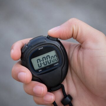 Close-up of a hand pressing the button on a digital stopwatch with a gray background