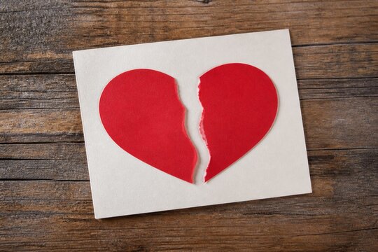 Red paper heart ripped in half on a white card over rustic wooden background