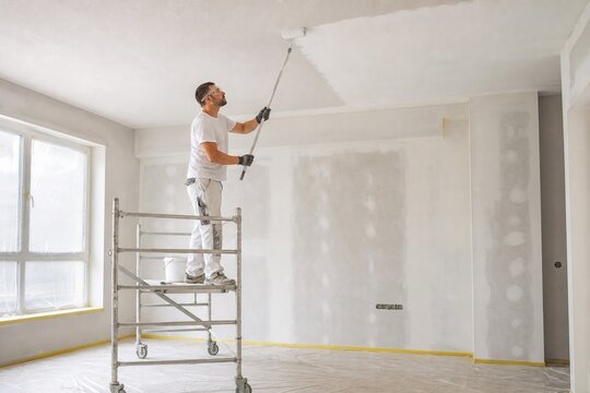 Professional painter applying primer to a ceiling with a roller from scaffolding