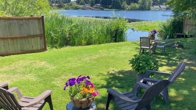 A peaceful backyard lawn overlooking a calm lake with lily pads, outdoor chairs, and colorful flowers.