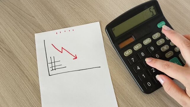 a paper with a falling red arrow chart and calculator calculations in the background, decreasing revenue, financial losses, low income and economic downturn.