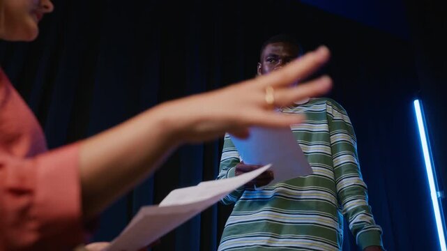 Caucasian young woman rehearsing script with African American young man on theater stage from low angle. Perfect for drama education and performing arts promotions