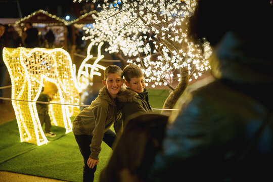 Mother photographing sons posing at glowing Christmas light display