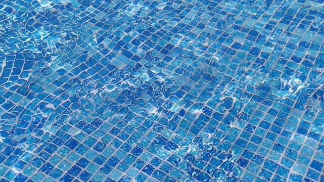 Clear blue water rippling in swimming pool with mosaic tile bottom. Sunlight reflections on water surface. Summer vacation, resort leisure and relaxation concept.