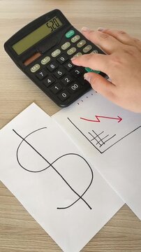 Papers with a US dollar symbol and a downward financial chart on a table, with a person calculating figures on a calculator, falling dollar exchange rate, currency decline, inflation and economic cris