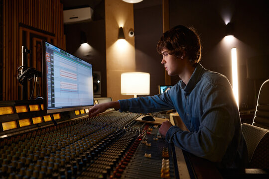 Music producer focuses deeply amidst ambient studio setting with equipment