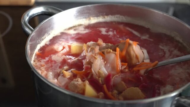 Close-up. Boiling borscht in a saucepan. A woman's hand stirs the borscht and meat with a spoon.