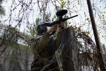 Obraz premium Confident soldier aims a paintball gun while hiding in the dry trees
