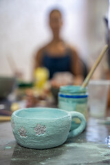 Handmade ceramic mug with floral decoration covered in glaze before kiln firing. Finished pottery piece represents craftsmanship, creativity and artisan ceramic production © dtatiana