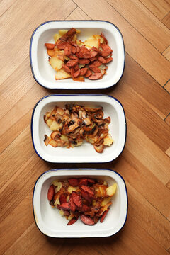 Fried potatoes with sausages and mushrooms in enamel dishes flat lay