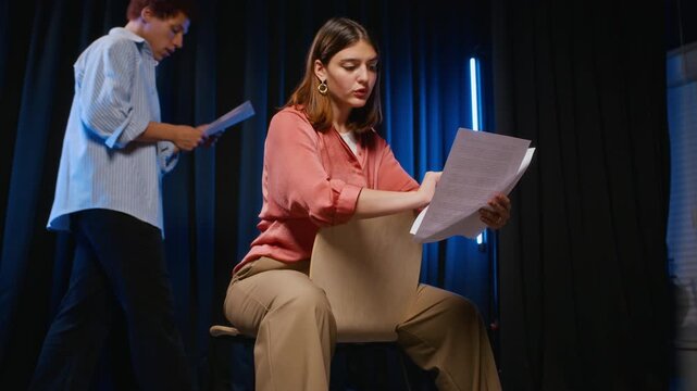 Caucasian teenage girl sitting on stage, reading script and rehearsing lines during theater class. Video suitable for drama school advertising and performing arts education projects