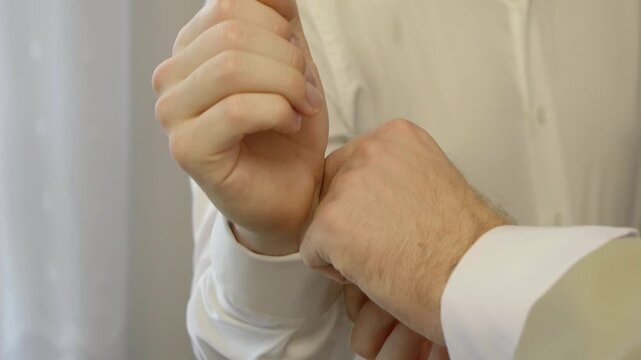 Best man helping the groom put on his cufflinks during the final wedding preparations.