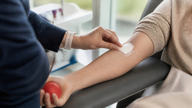 healthcare image showing the hands and forearm of a blood donor after donation, small medical dressing covering the venipuncture site, donation center environment