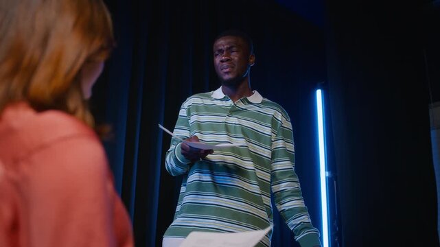 African American young adult actor rehearsing dramatic dialogue from script on stage with partner. Footage suitable for drama school promo and acting workshops