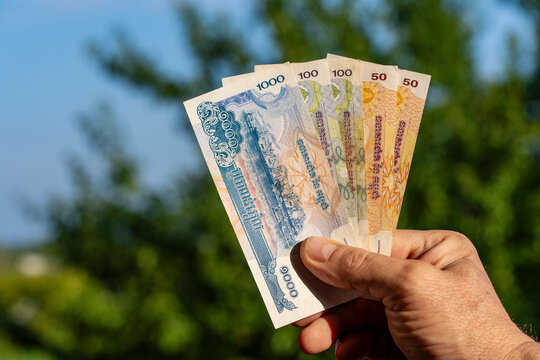 Hand holding Cambodian riel banknotes closeup. Male hand holds fan of Cambodian riel currency bills with denominations of 1000, 100, and 50 riels against blurred green nature background