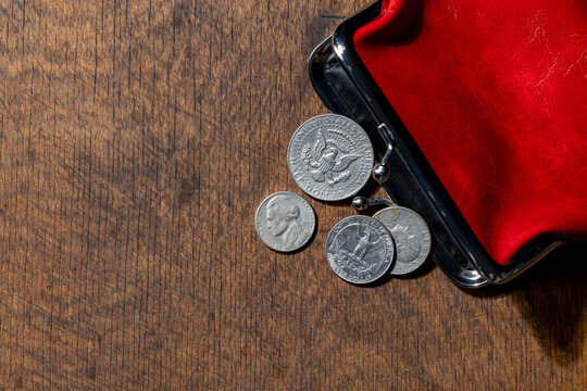 US dollar coins spilling from open red purse, closeup. Top view of American cents, including half dollar, quarter, and nickel, falling out of an open red leather coin purse on textured wooden table