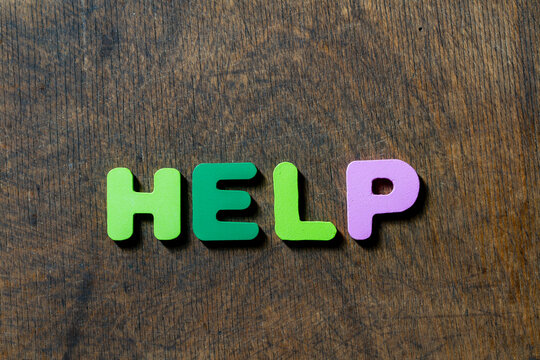 Word help written with colorful letters on wooden background. Word help spelled out using bright green and purple letters on textured brown wooden surface, creating clear conceptual message