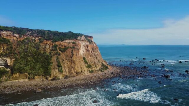 Stunning aerial shot of steep rocky cliffs meeting gentle ocean waves along a scenic coastline under a clear blue sky