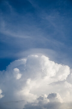Fluffy white cumulus cloud with pileus cap forming in deep blue sky background nature landscape close up daylight vertical view for background and copy space