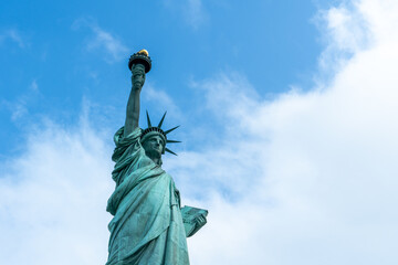 Statue of Liberty rising against a bright blue sky with soft white clouds, capturing freedom, democracy, travel, American heritage, tourism, and an iconic urban landmark in New York City. © byjeng