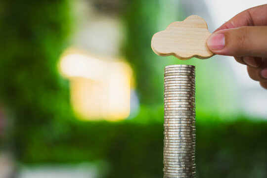 Cloud computing cost and weather insurance concept with hand placing wooden symbol on coin stack against green bokeh background for digital storage investment and saving for rainy days.