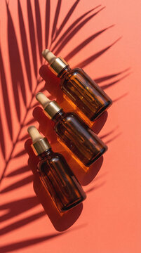 Three brown glass dropper bottles of serum or oil are arranged diagonally on a vibrant coral background with shadow from a palm branch. A tropical, summery, and luxurious ambiance.