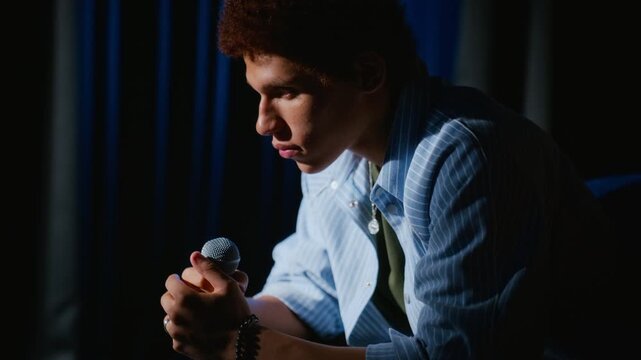 Biracial teenager holding microphone while rehearsing on stage with camera tilting up. Footage fits youth theater education, acting courses, and talent show campaigns