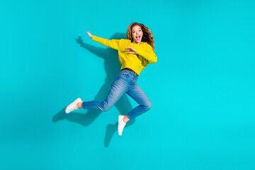 Fototapeta premium Young stylish woman wearing a yellow sweater jumps in the air against a blue background for a vibrant fashion lifestyle stock image