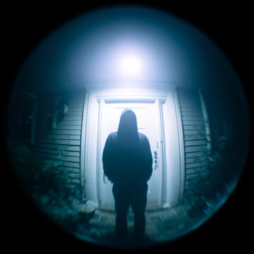 Silhouette of hooded figure at door