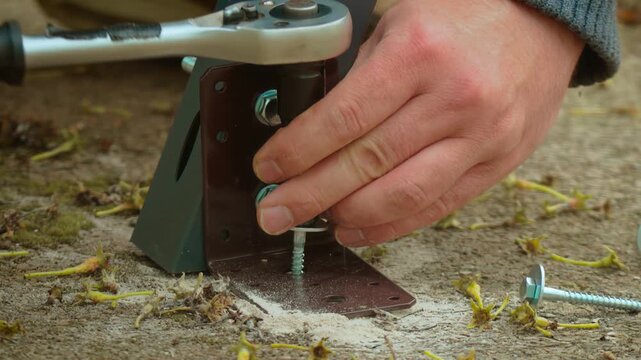 Ratchet wrench tightening screw into anchor through metal bracket on concrete surface close up. Hand applying torque while fastening structural support to masonry base with precision. Installation