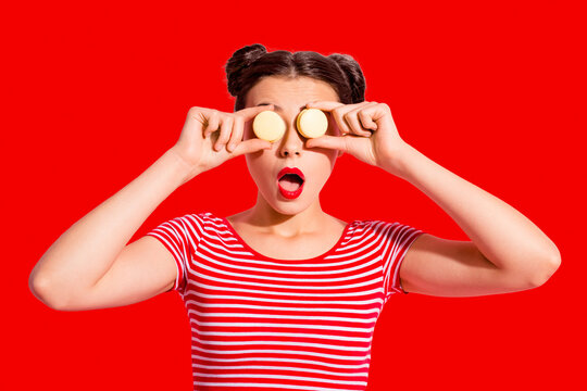 Close-up portrait of nice cute charming attractive glamorous lovely funny comic teen girl in striped t-shirt covering eyes with colorful delicious snack opened mouth isolated over pink background