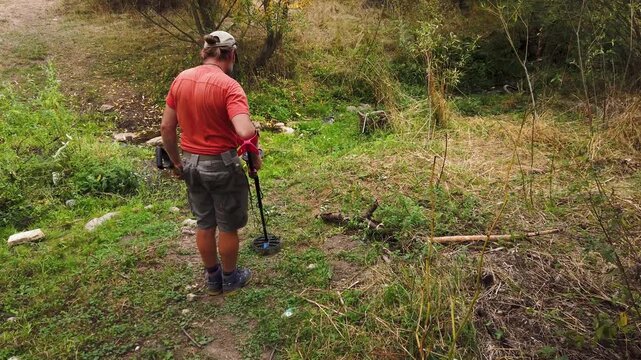 Treasure hunter with metal detector search coins in field 